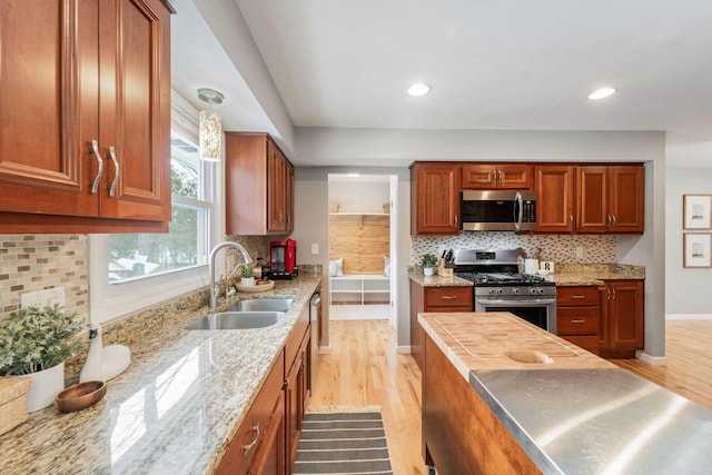 kitchen featuring light stone counters, stainless steel appliances, sink, and light wood-type flooring