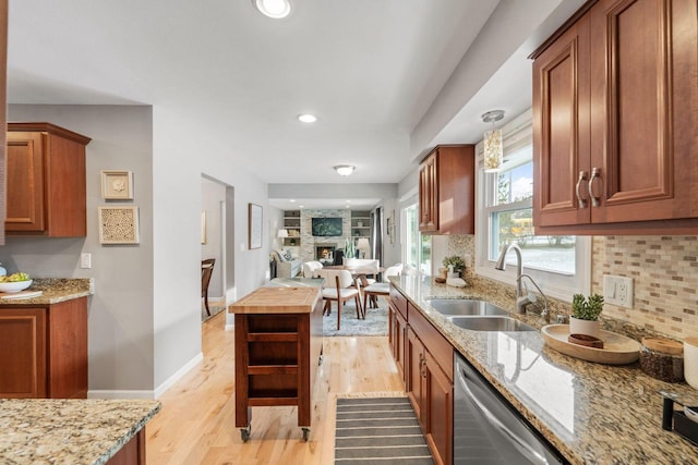 kitchen featuring tasteful backsplash, dishwasher, sink, a large fireplace, and light wood-type flooring