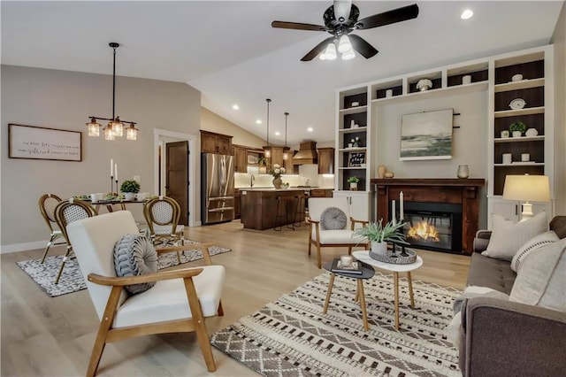 living area with a glass covered fireplace, ceiling fan, light wood-type flooring, and lofted ceiling