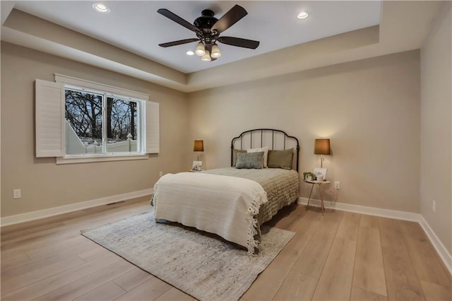 bedroom with light wood finished floors, recessed lighting, a tray ceiling, and baseboards