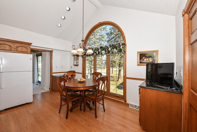 dining area with a chandelier, light hardwood / wood-style floors, a textured ceiling, and vaulted ceiling