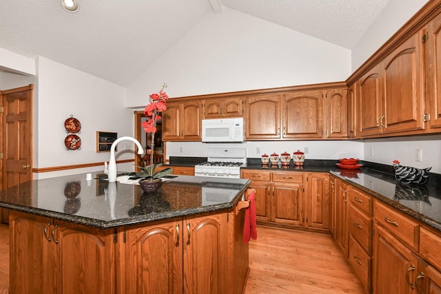 kitchen featuring sink, light hardwood / wood-style flooring, high vaulted ceiling, white appliances, and a kitchen island with sink