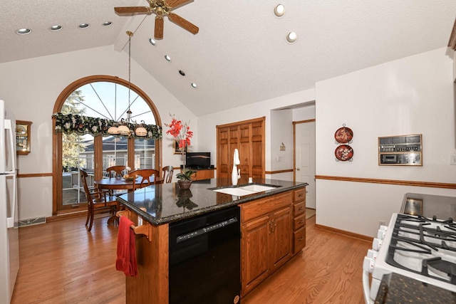 kitchen featuring light wood-type flooring, white appliances, sink, dark stone countertops, and a kitchen island