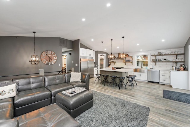 living room with light wood-type flooring, an inviting chandelier, vaulted ceiling, and sink