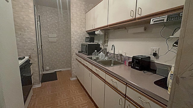 kitchen with parquet flooring, electric stove, white cabinetry, and sink