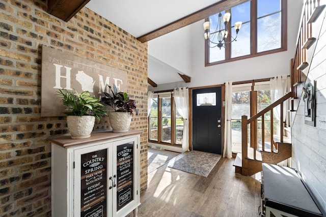 entryway featuring a high ceiling, brick wall, beam ceiling, a chandelier, and hardwood / wood-style floors