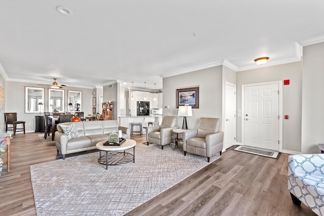 living room featuring ceiling fan, light wood-type flooring, and ornamental molding