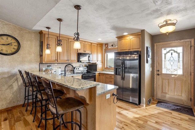 kitchen featuring kitchen peninsula, light stone countertops, light hardwood / wood-style flooring, and black appliances