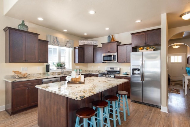 kitchen featuring a breakfast bar, hardwood / wood-style flooring, a kitchen island, dark brown cabinetry, and stainless steel appliances