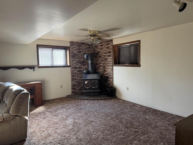 unfurnished living room featuring carpet flooring, ceiling fan, and a wood stove