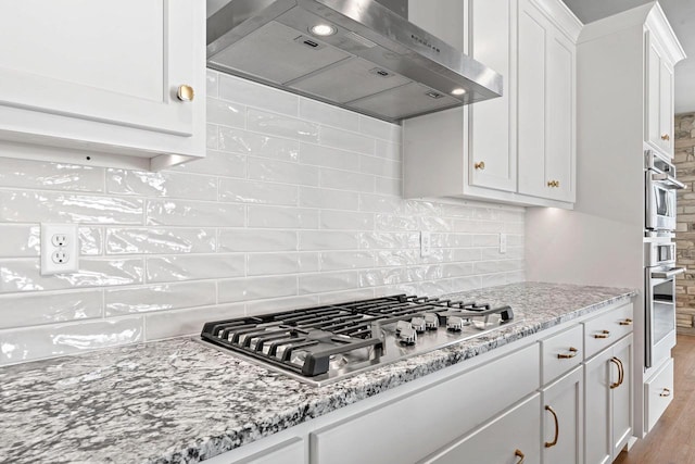 kitchen with light stone counters, light hardwood / wood-style floors, stainless steel gas cooktop, white cabinetry, and ventilation hood