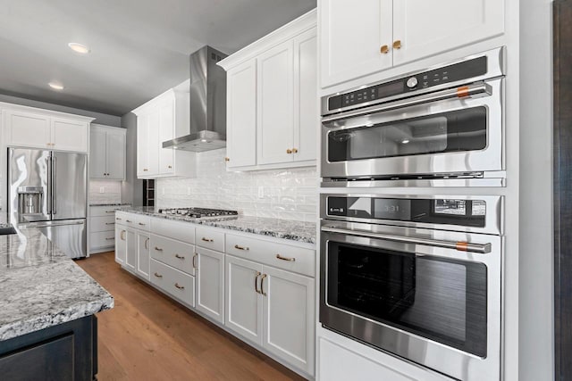 kitchen featuring appliances with stainless steel finishes, white cabinetry, tasteful backsplash, and wall chimney exhaust hood