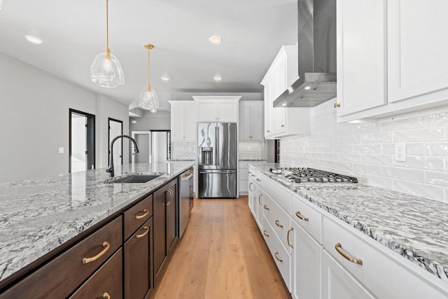 kitchen featuring sink, white cabinets, dark brown cabinets, wall chimney range hood, and appliances with stainless steel finishes