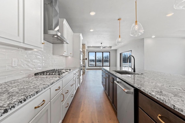 kitchen featuring sink, white cabinets, dark brown cabinets, wall chimney range hood, and appliances with stainless steel finishes