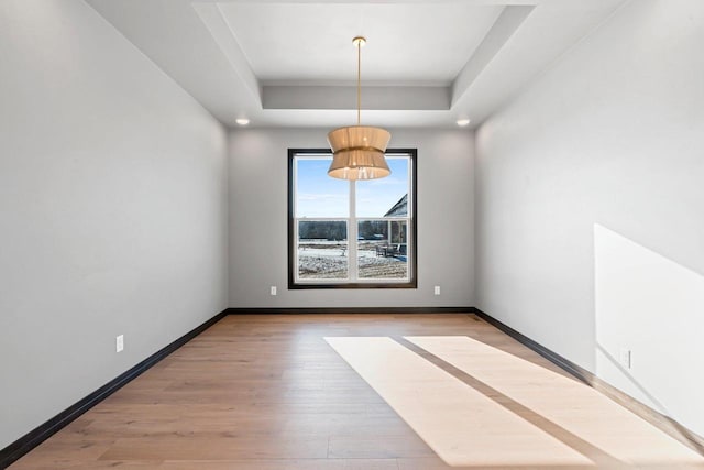 unfurnished dining area featuring light hardwood / wood-style floors and a tray ceiling