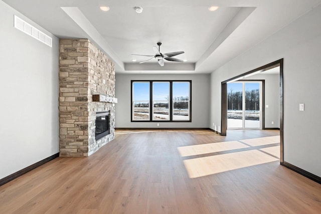 unfurnished living room with a raised ceiling, a fireplace, ceiling fan, and light hardwood / wood-style floors