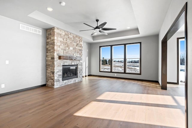 unfurnished living room featuring ceiling fan, a raised ceiling, a fireplace, and hardwood / wood-style flooring