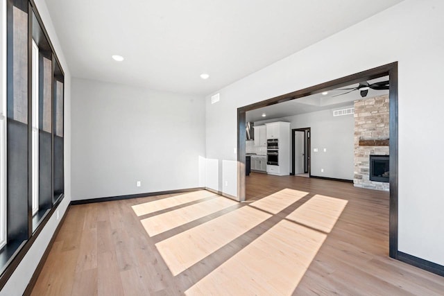 unfurnished living room with a fireplace, light wood-type flooring, and ceiling fan