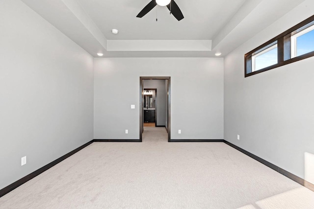 empty room featuring a raised ceiling, ceiling fan, and light carpet