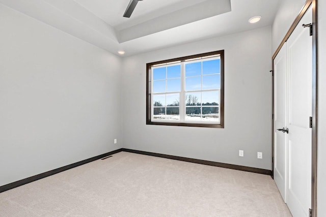 unfurnished bedroom with ceiling fan, light colored carpet, and a raised ceiling