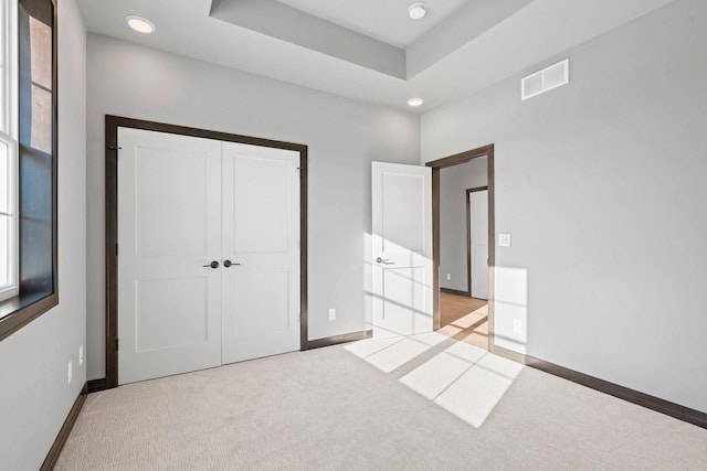 unfurnished bedroom featuring light colored carpet, a closet, and a tray ceiling