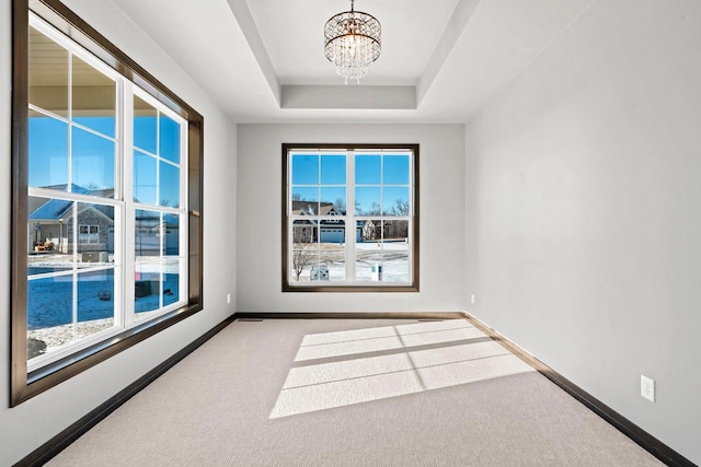 unfurnished room with an inviting chandelier, a tray ceiling, and carpet