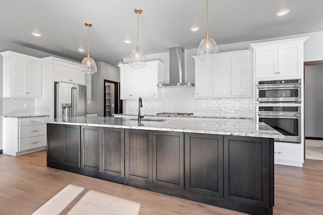 kitchen with decorative light fixtures, stainless steel appliances, wall chimney range hood, and white cabinets