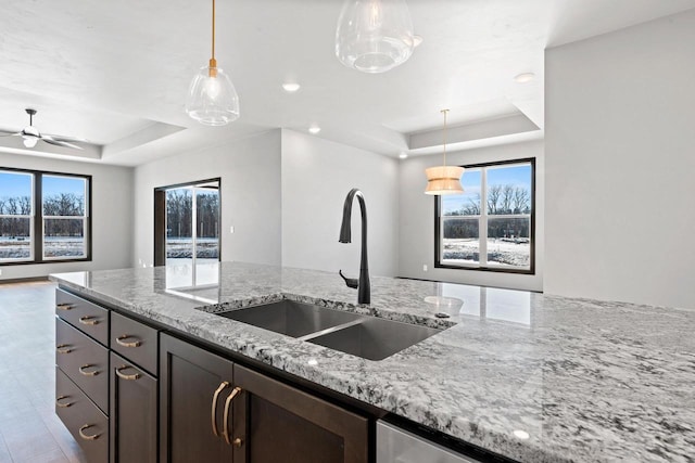 kitchen featuring light stone counters, ceiling fan, a raised ceiling, and sink