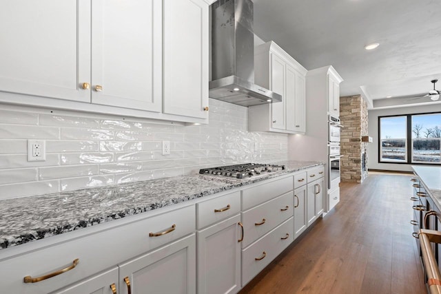 kitchen featuring stainless steel appliances, white cabinetry, light stone counters, dark hardwood / wood-style flooring, and wall chimney range hood