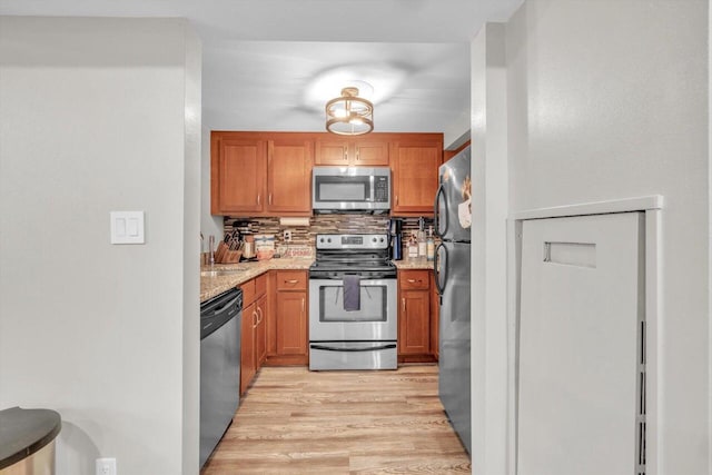 kitchen featuring decorative backsplash, light hardwood / wood-style flooring, light stone countertops, and appliances with stainless steel finishes