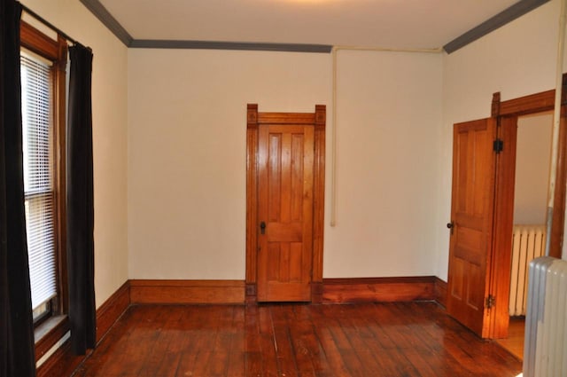 unfurnished room featuring dark hardwood / wood-style floors, radiator heating unit, crown molding, and a wealth of natural light