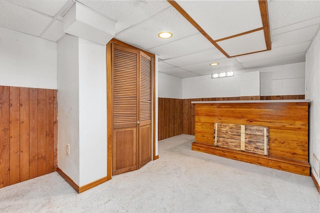 interior space with wooden walls, a drop ceiling, and light carpet