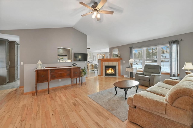 living room featuring ceiling fan, light hardwood / wood-style floors, lofted ceiling, and a tiled fireplace