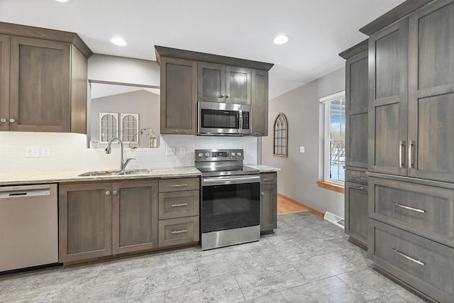 kitchen with appliances with stainless steel finishes, backsplash, light stone counters, and sink