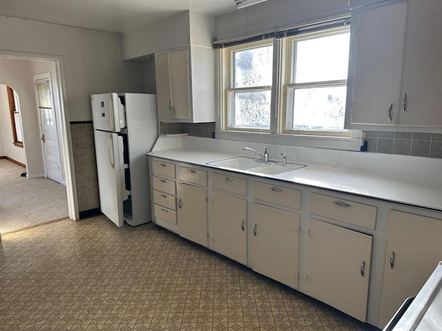 kitchen with white refrigerator, backsplash, white cabinetry, and sink