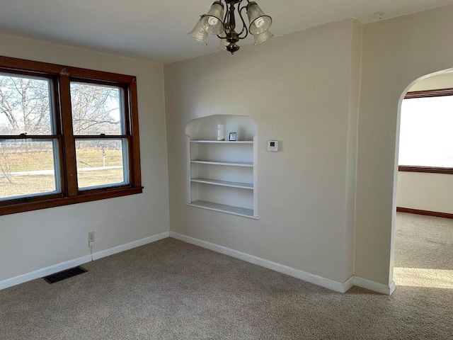 spare room with carpet flooring, built in shelves, and an inviting chandelier