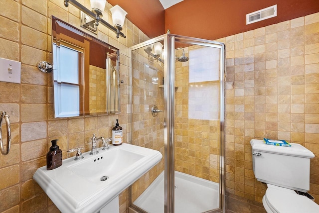 bathroom with toilet, decorative backsplash, tile walls, a shower with door, and sink