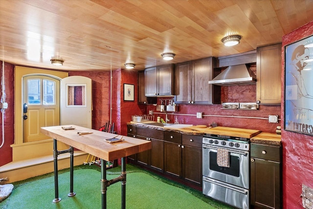 kitchen featuring stainless steel range with gas cooktop, wall chimney range hood, dark colored carpet, wooden ceiling, and sink