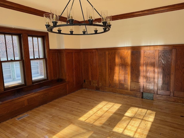 unfurnished dining area featuring wood walls, light hardwood / wood-style flooring, and an inviting chandelier