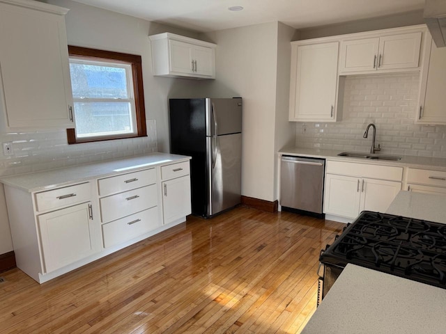 kitchen with sink, stainless steel appliances, tasteful backsplash, light hardwood / wood-style floors, and white cabinets