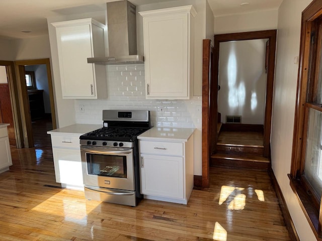 kitchen featuring light wood-type flooring, white cabinetry, stainless steel range with gas cooktop, and wall chimney exhaust hood