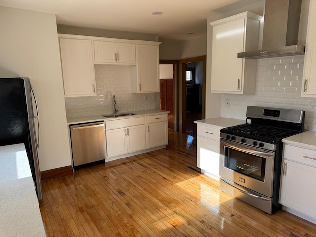 kitchen featuring light wood-type flooring, wall chimney exhaust hood, stainless steel appliances, sink, and white cabinetry