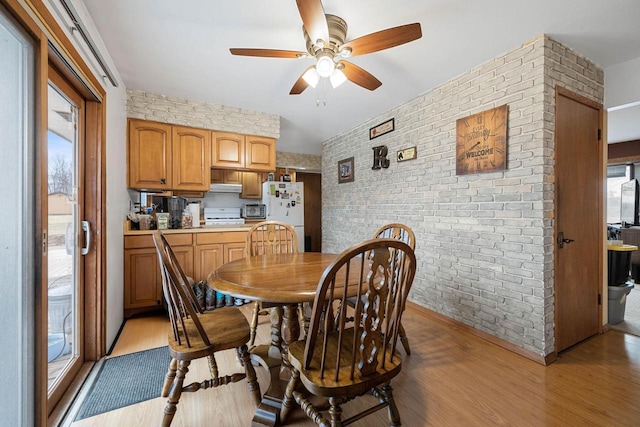 dining room featuring ceiling fan, light hardwood / wood-style floors, and brick wall