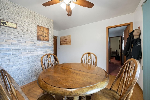 dining space with hardwood / wood-style floors, ceiling fan, and brick wall