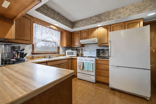 kitchen featuring kitchen peninsula, brick wall, white appliances, sink, and light hardwood / wood-style flooring