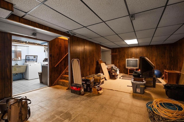 basement featuring a paneled ceiling, wood walls, sink, and washer / clothes dryer