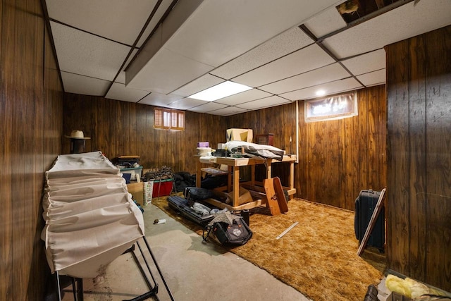 basement featuring carpet flooring, wood walls, and a drop ceiling