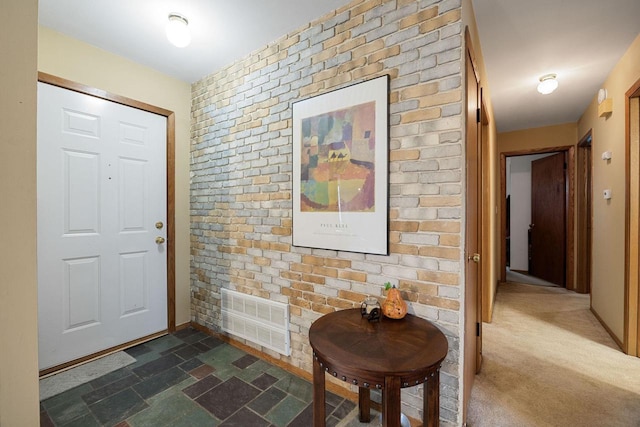 carpeted entryway featuring brick wall