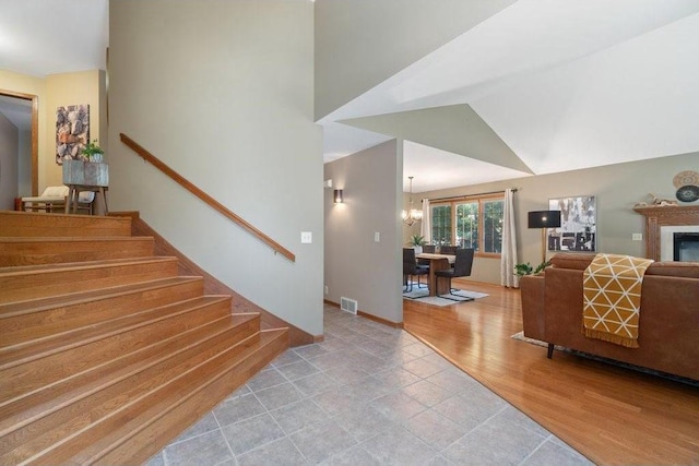 stairs with a notable chandelier, wood-type flooring, and vaulted ceiling