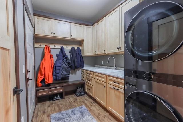 clothes washing area with cabinets, sink, stacked washing maching and dryer, and light hardwood / wood-style floors